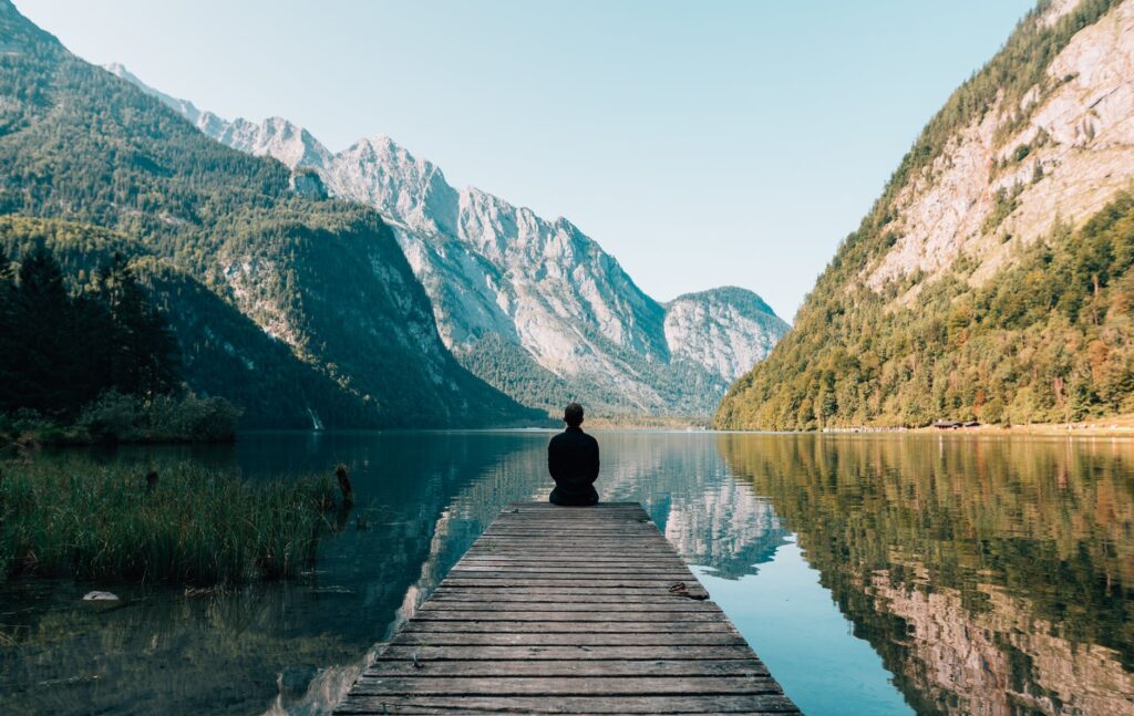 a person sitting on wooden planks across the lake scenery